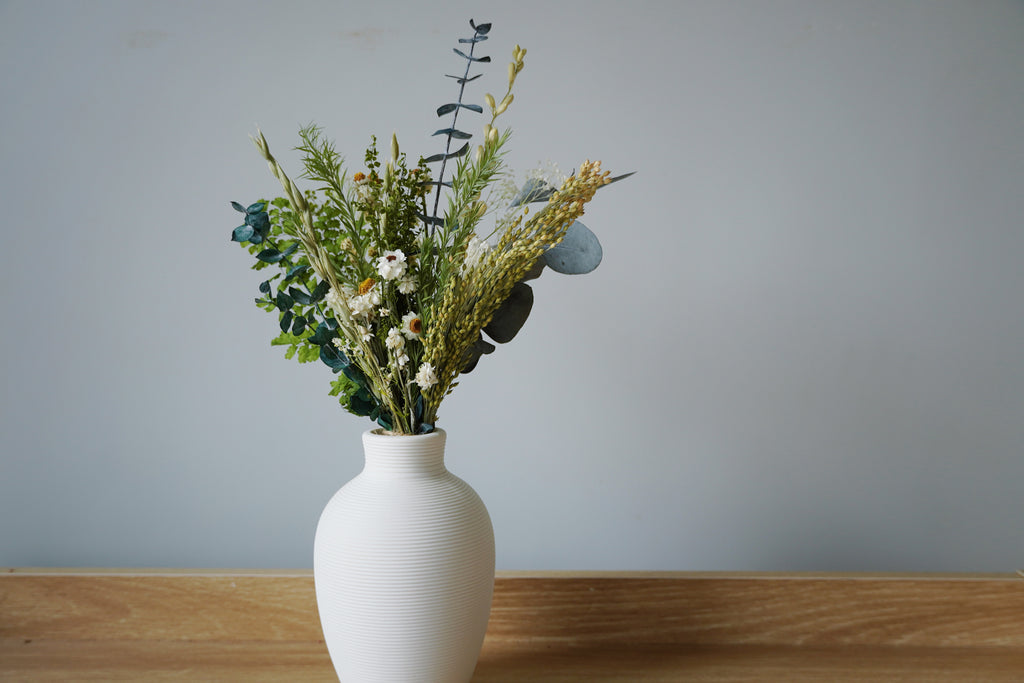 White vase with greenery on a wooden surface against a gray wall