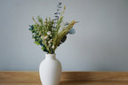 White vase with greenery on a wooden surface against a gray wall