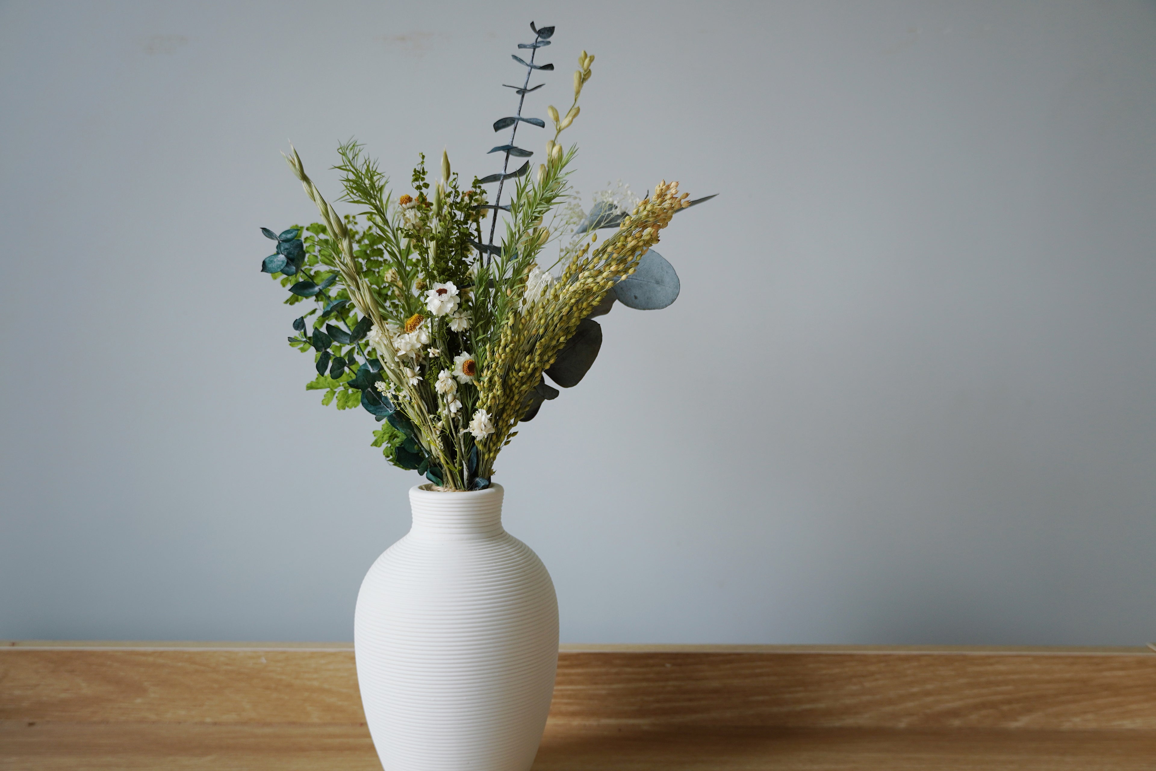 White vase with greenery on a wooden surface against a gray wall