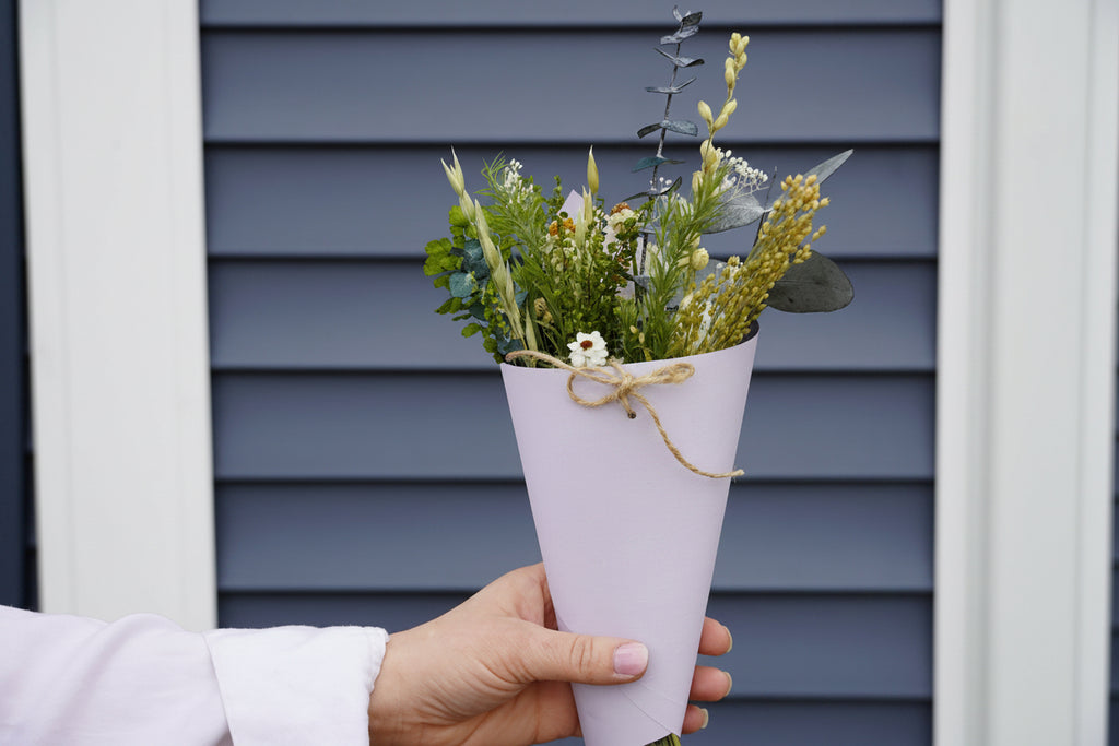 Hand holding a small bouquet of flowers with a 'honey moon' tag against a blue wall.
